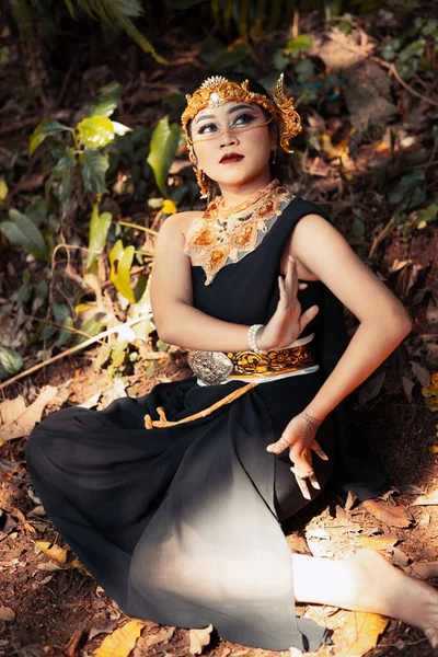 森の中で黄金の冠と黄金のネックレスを身に着けている間 インドの女性は彼女の顔に黒いドレスと化粧で座っている — ストック写真