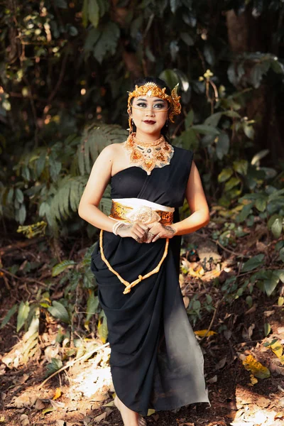 村の森の中に黄金の冠と黄金の鎖を身に着けている間 黒いドレスに身を包んだ美しいアジアの女性 — ストック写真