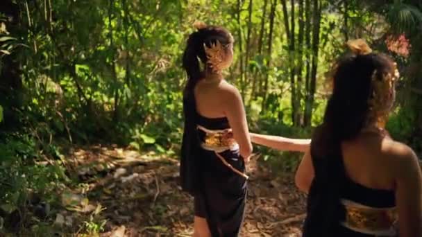 美丽的巴厘女人 头戴金色的皇冠 身穿黑色的连衣裙 面带笑容地在村子里的森林边奔跑着 — 图库视频影像
