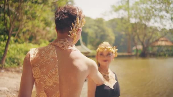 村の中に幸せな顔を持つ湖の近くに黄金の冠と黒のドレスを持つ美しい女性を迎えるアジアの男 — ストック動画