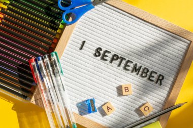 1 Eylül 'de okul malzemelerini kalem, makas, ABC ve sarı arka planda boya olarak içeren bir pano. Eğitim. Bilgi günü, ders çalışma, okul konseptine dönüş.