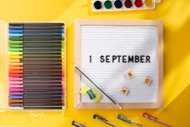 1 Eylül 'de okul malzemelerini kalem, makas, ABC ve sarı arka planda boya olarak içeren bir pano. Eğitim. Bilgi günü, ders çalışma, okul konseptine dönüş.