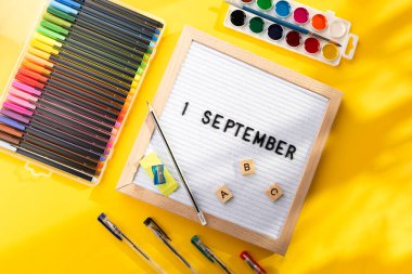 1 Eylül 'de okul malzemelerini kalem, makas, ABC ve sarı arka planda boya olarak içeren bir pano. Eğitim. Bilgi günü, ders çalışma, okul konseptine dönüş.