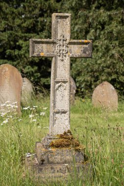 Mezarlıkta haç şeklinde bir mezar taşı. Uzun yeşil çimenlerde.