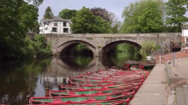 Man running across bridge with arches over river Nidd and red paddle boats moored in the river in knaresborough, Yorkshire, UK