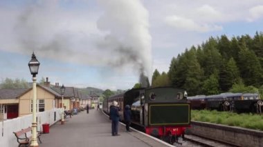  People talking to steam train driver from platform while train is blowing white and black smoke at Bolton Abbey Steam Railway, Yorkshire,UK