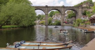 Two people and dog in small tourist boat on the River Nidd near Knaresborough viaduct