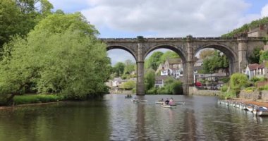 People enjoying a relaxing leisure tourist boat ride, paddling on the River Nidd near Knaresborough viaduct