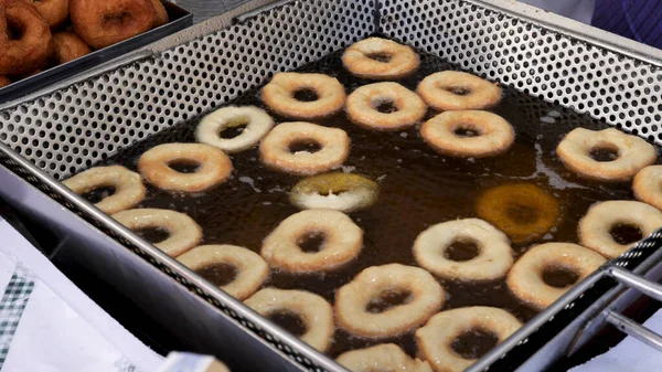 Donuts cooking in hot oil. Process of frying junk food at a food market.