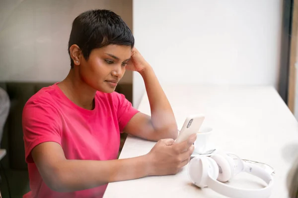 Pensive asian woman holding mobile phone reading text message, shopping online in modern cafe. Beautiful Indian student studying, distance learning, online education concept