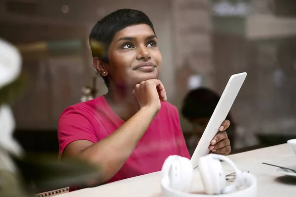 Beautiful pensive Indian woman using digital tablet shopping online, choosing something sitting in modern cafe. Asian student studying, distance learning, online education