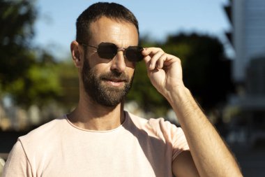 Yakışıklı, sakallı, şık güneş gözlüğü takan, caddeye bakan İspanyol. Yaz konsepti 