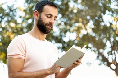 Yakışıklı orta yaşlı adam parkta kitap okuyor, boşluğu kopyalıyor.  