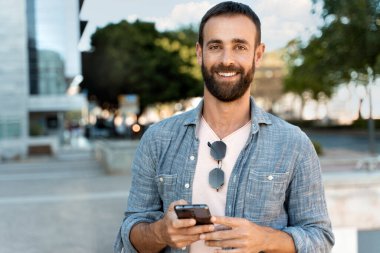 Çevrimiçi mobil uygulama alışverişi yapan yakışıklı, orta yaşlı bir adam. Şehir sokağındaki kameraya bakıyor. Mobil bankacılık kavramı  