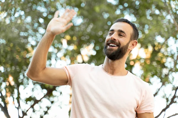 Smiling Bearded Hispanic Man Waving Hand Looking Away Standing Park — Stockfoto