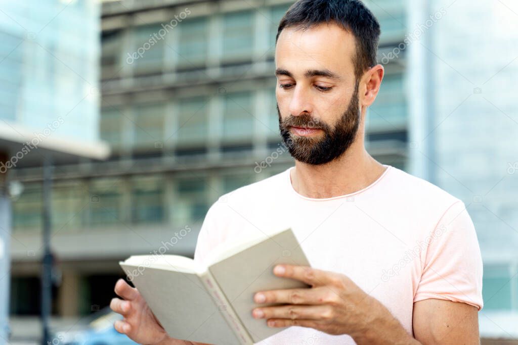 Handsome bearded hispanic man reading book outdoors. Pensive student studying, learning something, exam preparation, education concept