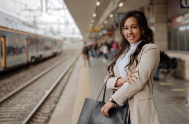 Başarılı gülümseyen iş kadını tren istasyonunda duruyor, kopyalama alanı. Tren beklerken kameraya bakan şık turist çantasıyla mutlu. Ulaşım, seyahat kavramı