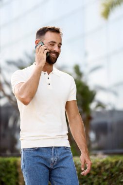 Kendine güvenen, gülümseyen, cep telefonuyla konuşan, caddede yürüyen, başka tarafa bakan Latin adam.