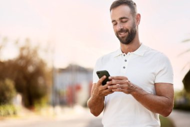 Handsome smiling latin man using mobile phone shopping online, reading text message, checking email on the street., copy space. E-commerce, mobile banking concept