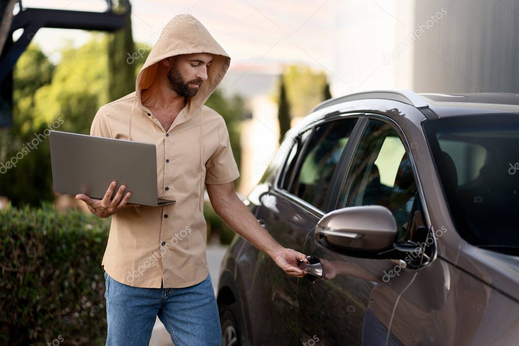 Bearded latin man trying to steal car using laptop and hacker software. Crime, carjacking concept