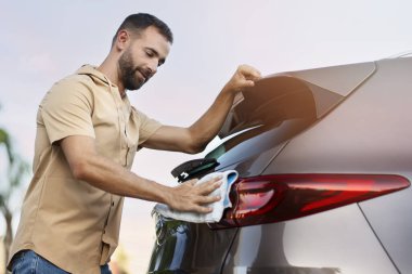 Yakışıklı latin adam mikro fiber bez kullanarak arabasını temizliyor. Araba yıkama servisi konsepti