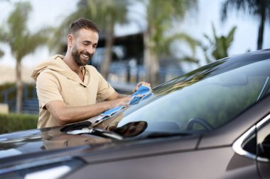 Portrait of smiling latin man cleaning car using micro fiber cloth. Car washing service concept
