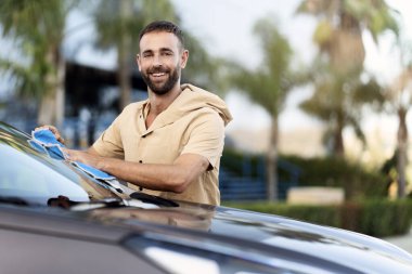 Güler yüzlü İspanyol adam mikro fiber bez kullanarak arabayı temizliyor. Araba yıkama servisi konsepti, kopyalama alanı