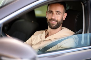 Portrait of confident smiling latin man driving a car looking at camera. Car sharing concept
