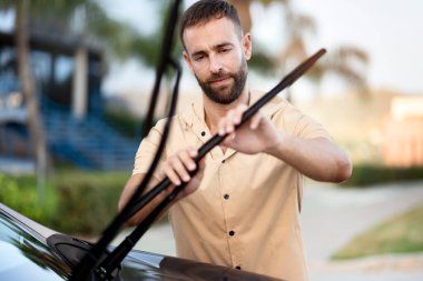 Düşünceli adam dışarıda duran arabanın sileceklerini değiştiriyor. Araba servisi kavramı