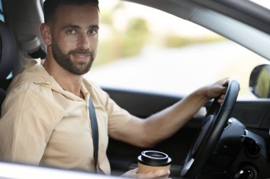 Elinde kahve bardağıyla gezen yakışıklı, gülümseyen Latin adamın portresi. Ulaşım, yolculuk, araba paylaşım konsepti