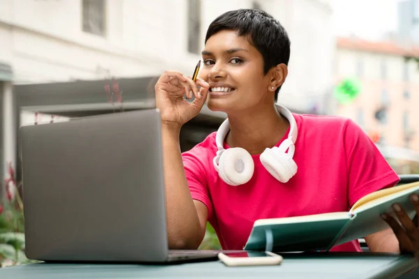 Portrait of beautiful smiling Indian student studying, using laptop computer, looking at camera. Asian freelancer working online sitting at workplace. Successful business