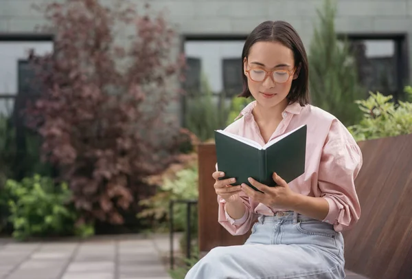 Mooie Pensive Aziatische Vrouw Dragen Stijlvolle Bril Leesboek Zittend Bank — Stockfoto