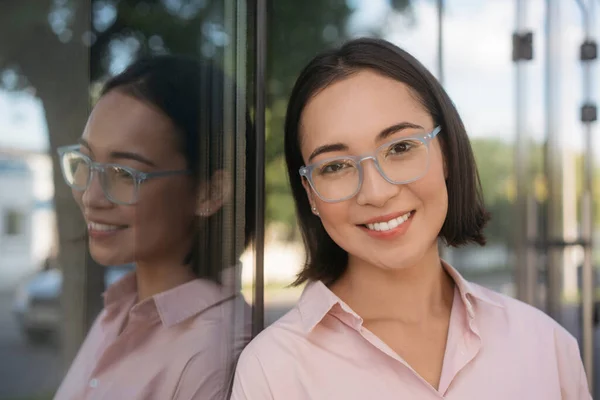 Smiling beautiful asian woman wearing stylish eyeglasses looking at camera on the street. Authentic portrait of happy successful university student, education concept