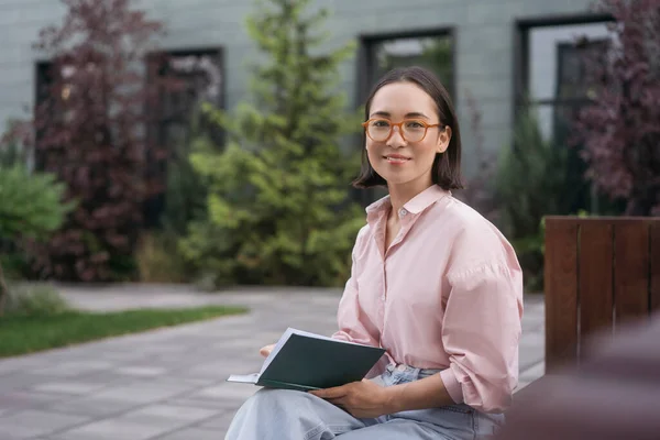 笑顔のアジア人留学生の肖像画 大学のキャンパスで言語を学ぶ 教育の概念 スタイリッシュな眼鏡をかけて美しい女性はベンチに座って本を読んで スペースをコピー — ストック写真