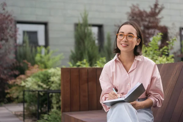 Portrait Confident Smiling Asian Writer Taking Notes Looking Away Sitting — Stock Photo, Image