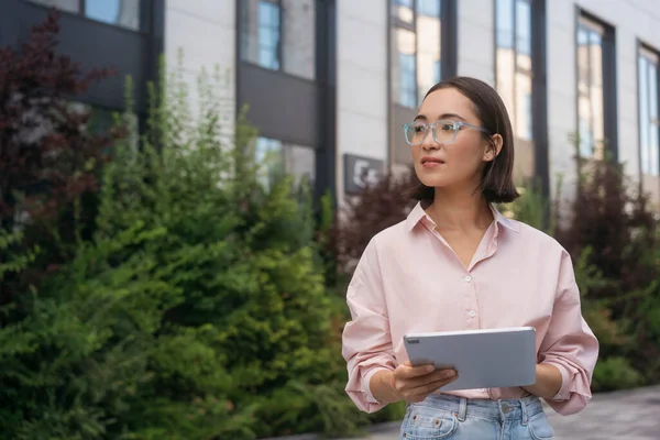 眼鏡をかけデジタルタブレットを持っているアジアのビジネス女性がオンラインで仕事を離れて通りに立って見て スペースをコピー — ストック写真