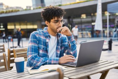 Zeki düşünceli ortadoğu öğrencisi, sınav hazırlığı, online eğitim konsepti. Yakışıklı adam dizüstü bilgisayar kullanıyor, online çalışıyor, iş yerinde eğitim kursları izliyor.