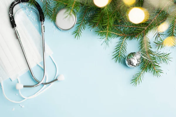 Medisch kerstconcept met stethoscoop, gezichtsmasker en kerstboom op blauw Stockfoto