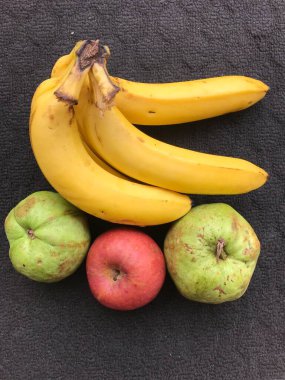 Bir demet muz, iki guava ve koyu arkaplanda bir elma.