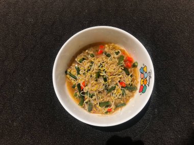 Siyah arka planı olan beyaz bir kabın içinde fasulye filizleniyor.