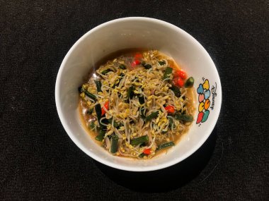 Siyah arka planı olan beyaz bir kabın içinde fasulye filizleniyor.