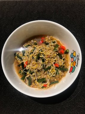 Siyah arka planı olan beyaz bir kabın içinde fasulye filizleniyor.