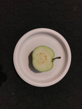 Koyu bir arka planda izole edilmiş pembe plastik bir tabakta guava dilimi.