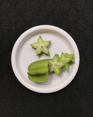 Yeşil yıldız meyve dilimleri pembe plastik bir plaka üzerinde koyu bir arka planda izole edilmiş.