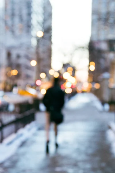 Intentionally blurred rear view of a person walking down a city street in winter with reflections and bokeh background.