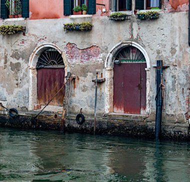 Venedik, İtalya 'da su yansıtan bir kanalda kapıları ve pencereleri olan eski renkli bir binanın ön cephesini kapatın..
