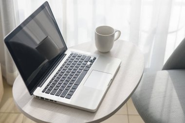 laptop and coffee cup on table and chair in bedroom