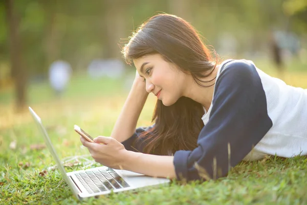 Attractive girl play mobile phone with laptop in garden