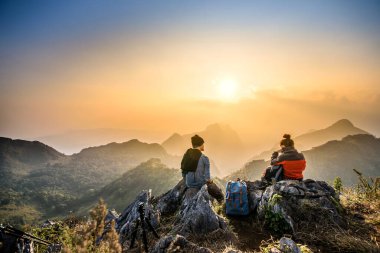 couple hiking at sunset mountain with heavy backpack golden hour