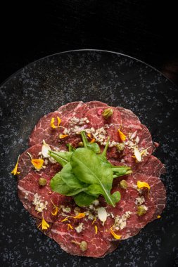 Sliced salami with vegetables on a black plate